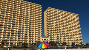 Ein Hochhaus-Hotel mit mehreren Balkonen und einem Strandbereich mit Sonnenschirmen.