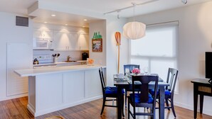 Une cuisine moderne avec des meubles blancs, un îlot central et un coin repas agrémenté de chaises bleues et d’une table.