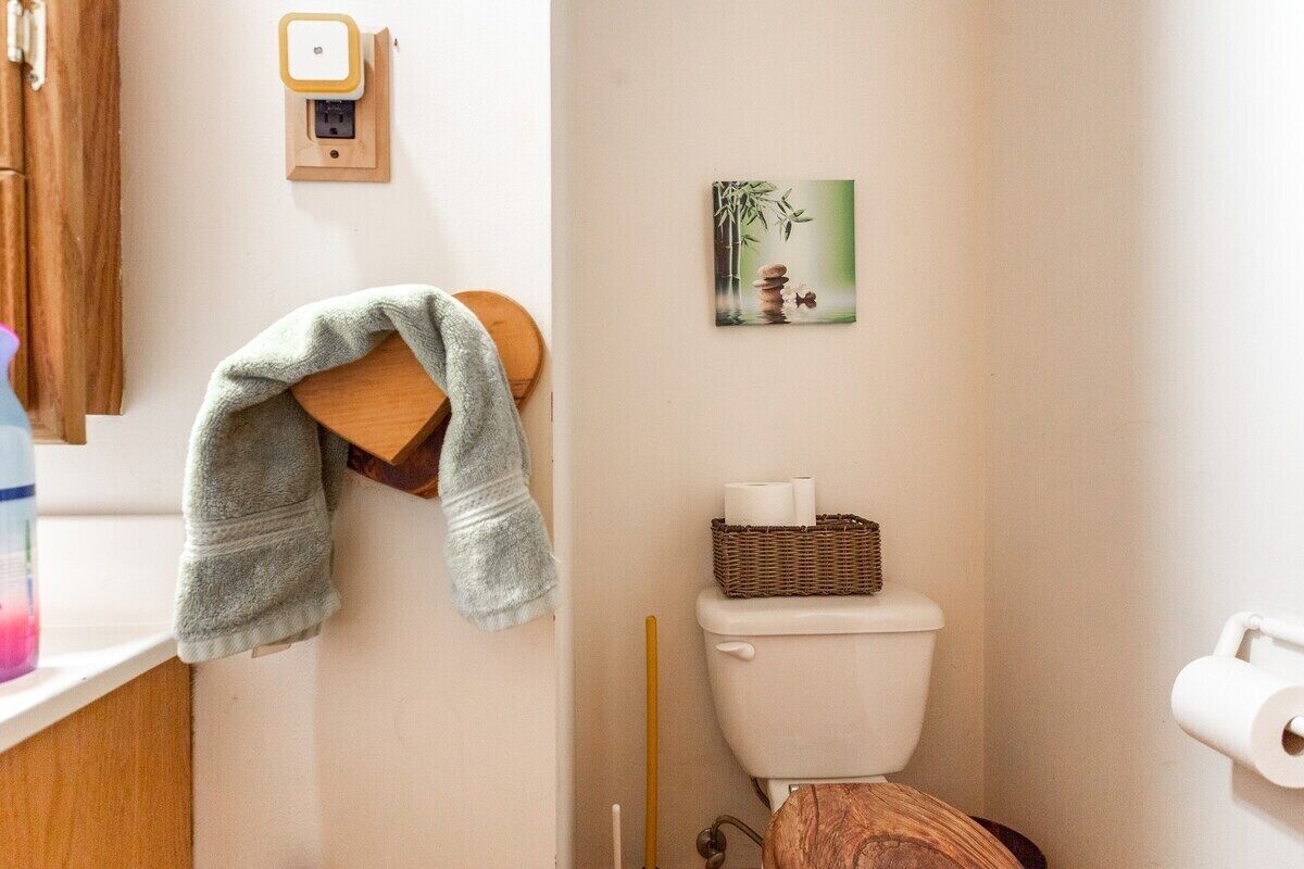 Een badkamer met een toilet, een handdoekrek met een handdoek, een foto aan de muur en een mand met toiletpapier.