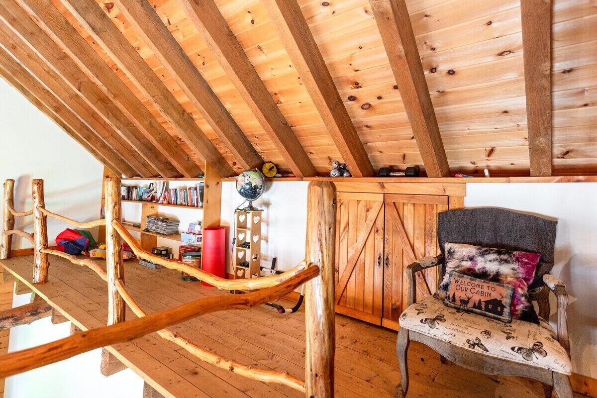 Interior rústico de una cabaña con techo de madera, una estantería, un escritorio y una silla con cojín.