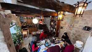 A rustic dining area with a stone wall, wooden beams, and a tiled floor. There is a round table with chairs, a potted plant, and various kitchen items in the background. - "La Bouyerie" cottage in a lovely setting, open countryside, breathtaking view (Najac)