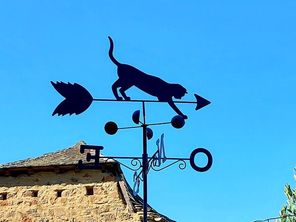En vejrhane med silhuet af en hund og et løvdesign, monteret på en bygning med en murstensfacade.