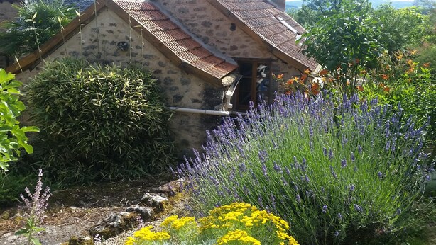 A stone house with a sloped roof, surrounded by various plants and flowers. - "La Bouyerie" cottage in a lovely setting, open countryside, breathtaking view (Najac)