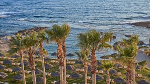 A beachside resort with palm trees, lounge chairs, and thatched umbrellas. - Atlantica Golden Beach -Adults Only (Kissonerga)