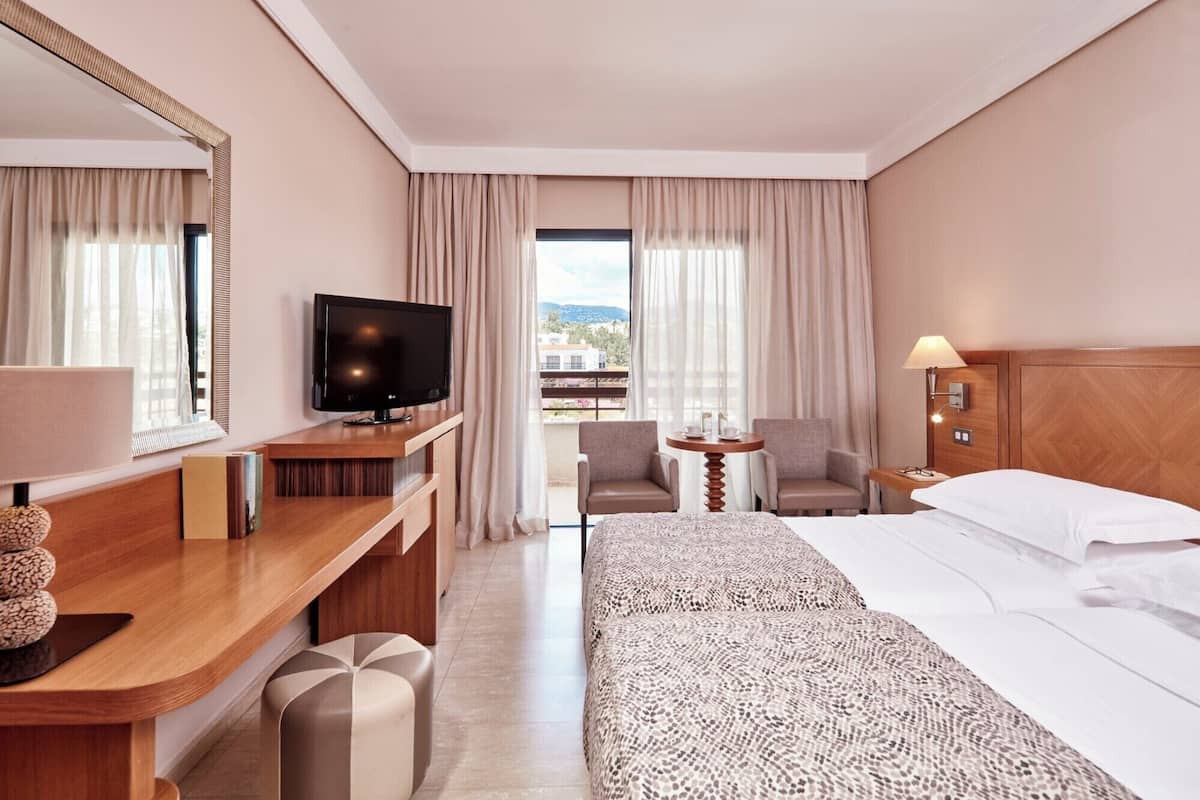 Habitación de hotel con cama, escritorio con televisor, silla, mesita y lámpara.