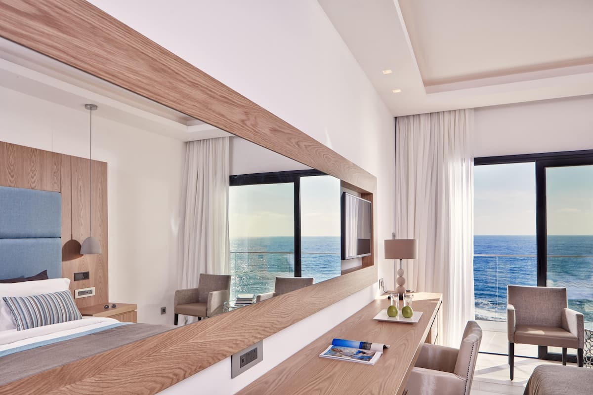 A modern hotel room with a large bed, a wooden desk, and a view of the ocean.