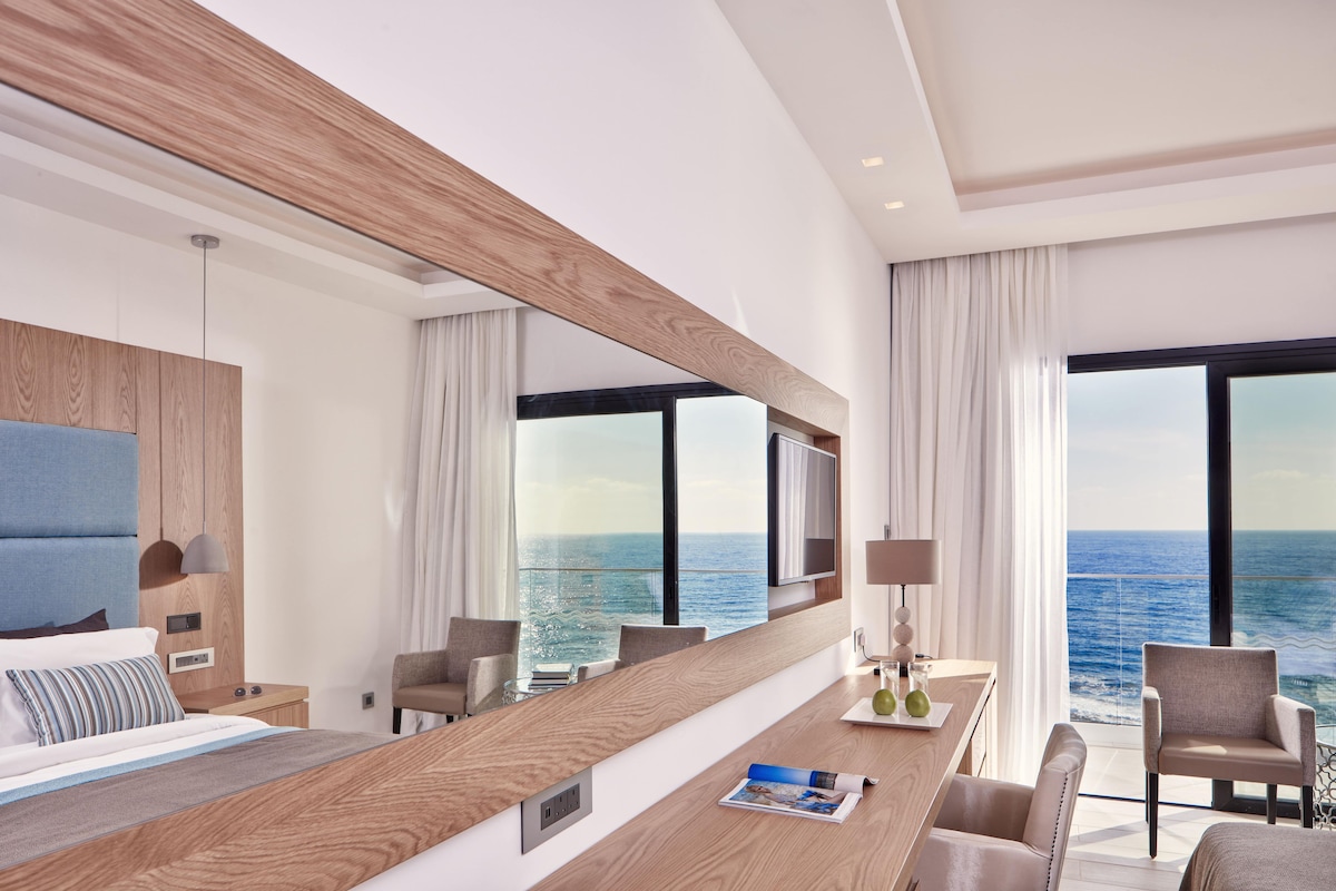 Habitación de hotel moderna con una cama grande, un escritorio de madera y vista al océano.