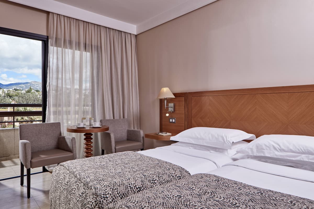 A hotel room with a bed, a chair, a small table, and a lamp.