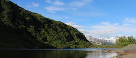 A calm lake with a forested hillside and snow-capped mountains in the background.