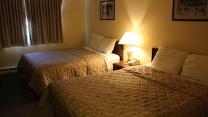 Een hotelkamer met twee bedden, een nachtkastje met een lamp en een raam met gordijnen.