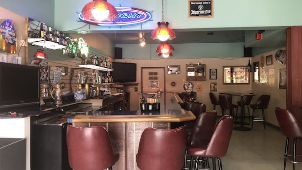 Een bar met een neonbord, meerdere hangende lampen en een verscheidenheid aan flessen en glazen op planken.