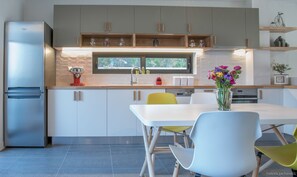 Una cocina moderna con un refrigerador de acero inoxidable, gabinetes blancos, una encimera de madera y un comedor con mesa blanca y sillas amarillas.