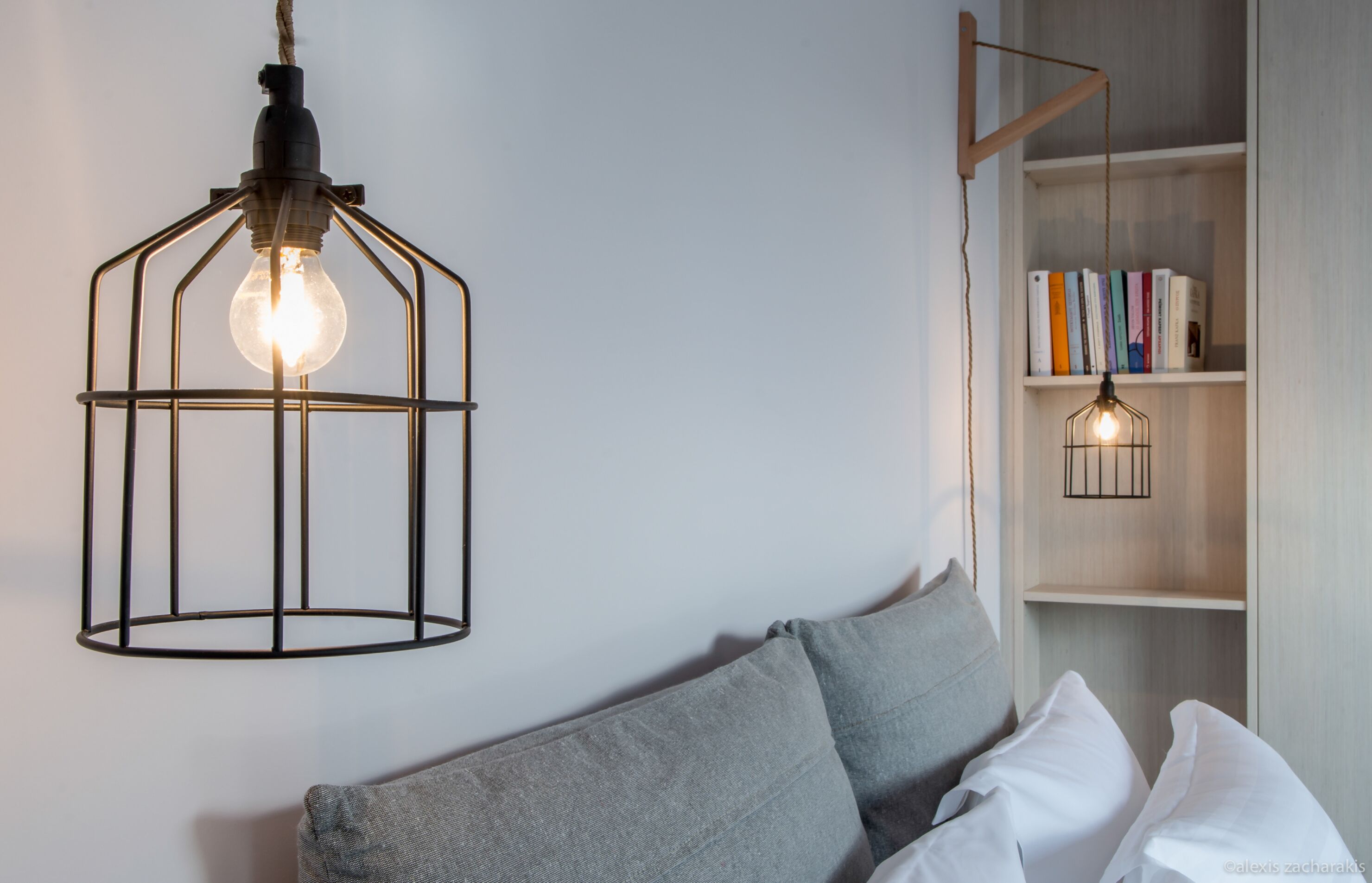 Una sala de estar moderna con un sofá gris, una estantería llena de libros y dos lámparas colgantes con bombillas a la vista.