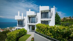 A modern white building with multiple balconies and a spiral staircase, overlooking a coastal area.