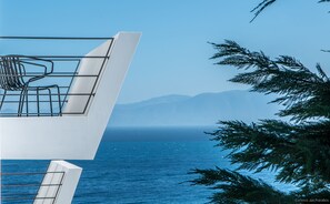 Un edificio moderno con un balcón que da a un cuerpo de agua y montañas distantes.