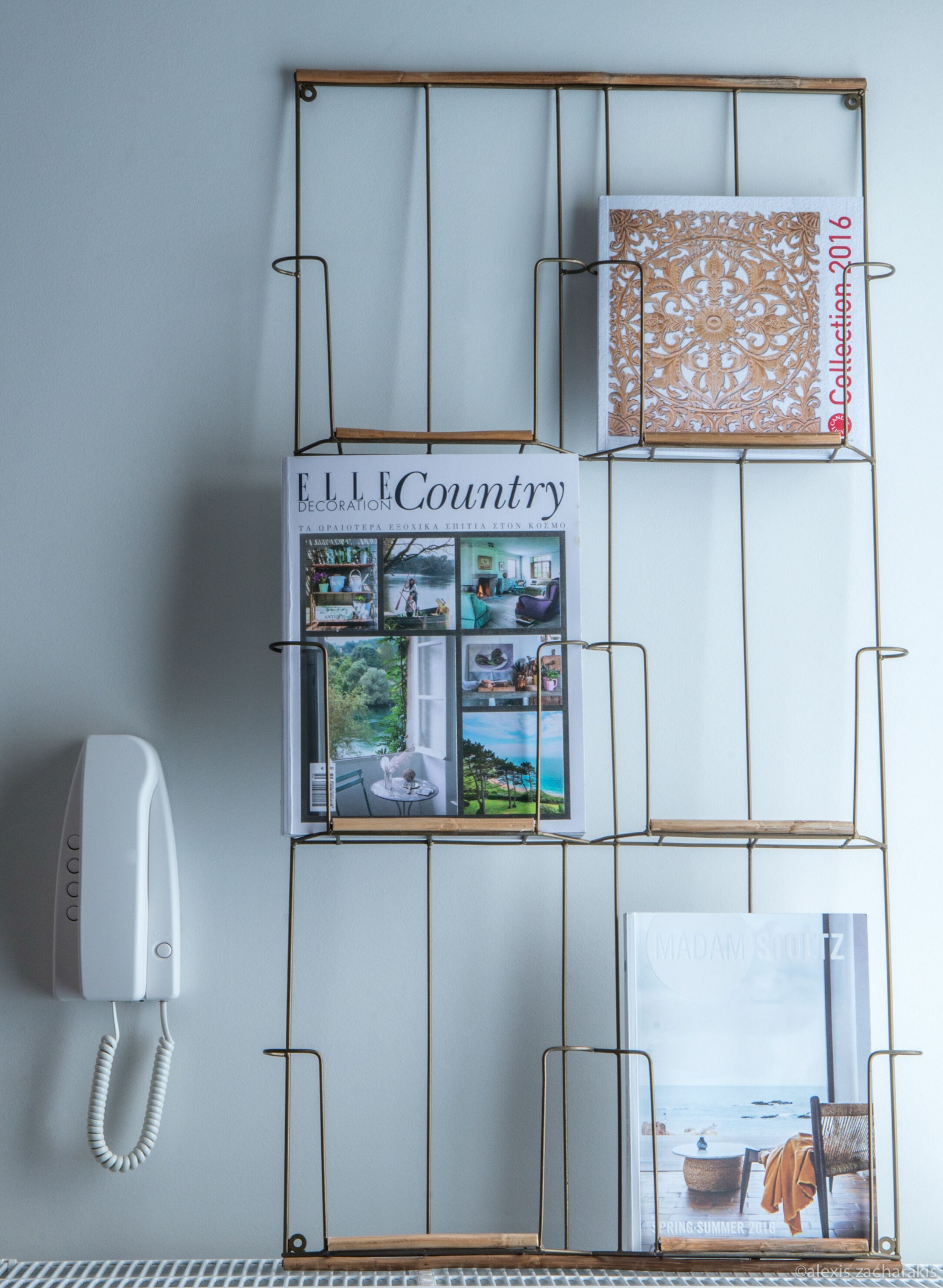 Un présentoir mural avec un magazine intitulé « ELLE Country » présentant des articles sur la décoration intérieure, une photographie encadrée d’un paysage côtier et une boîte décorative.
