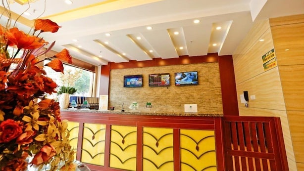 A reception area with a wooden reception desk, a large vase of flowers, and a wall-mounted TV screen. - Greentree Alliance Guangdong Shenzhen Foyong Subw (SHENZHEN)
