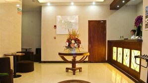 A lobby with a reception desk, a round table with a floral centerpiece, and a logo on the floor.