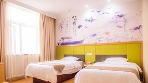 A hotel room with two beds, a wooden floor, a window with curtains, and a wall with artwork.