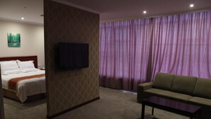 A hotel room with a bed, a television mounted on the wall, a sofa, and a coffee table.