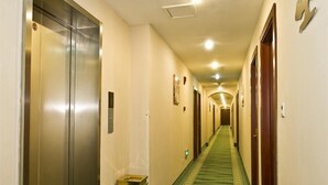 A hotel hallway with a carpeted floor, doors on both sides, and a trash bin.
