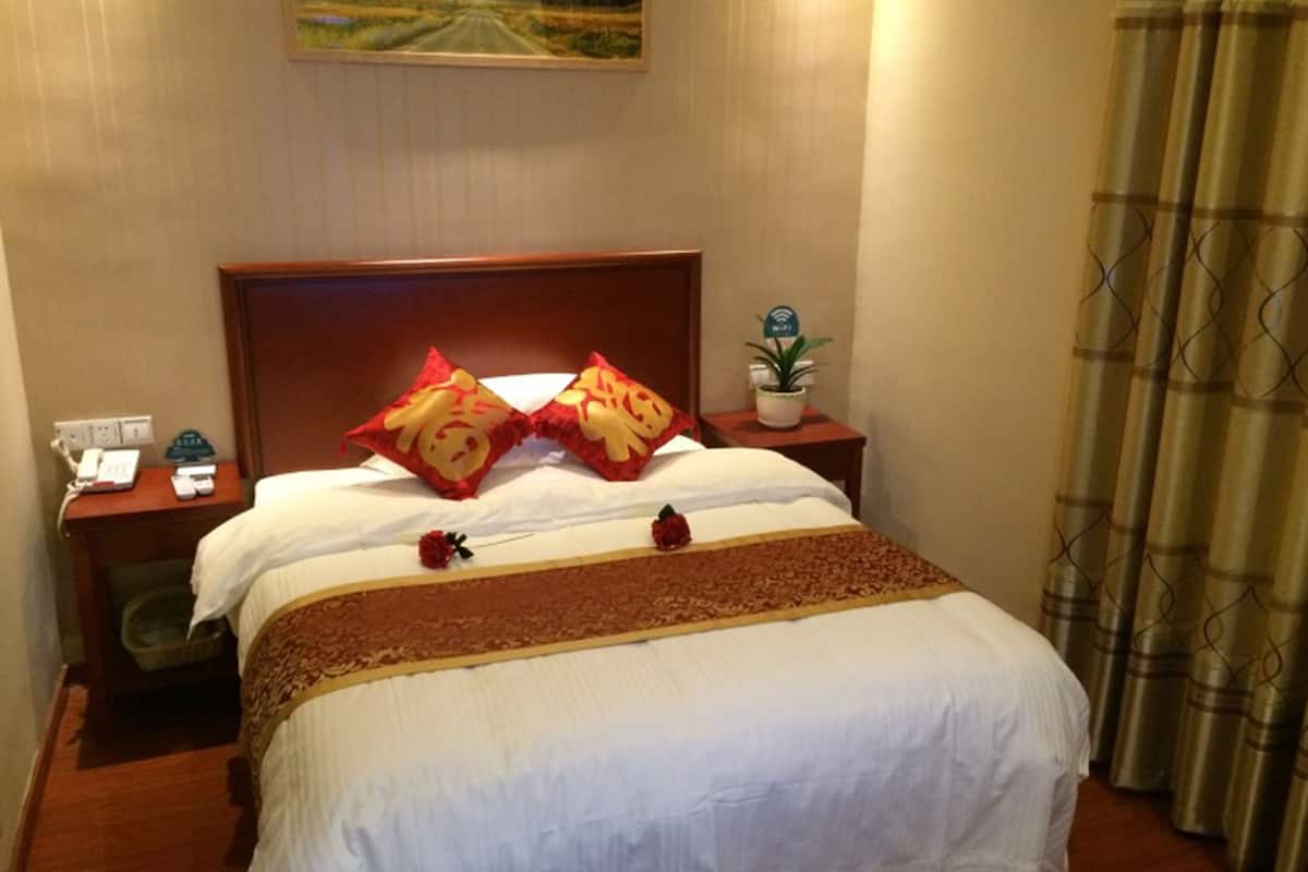 Ein Hotelzimmer mit einem großen Bett, zwei Nachttischen, einem Beistelltischchen mit Telefon, einer kleinen Topfpflanze und einem Bild an der Wand.