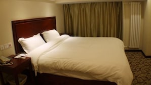A hotel room with a large bed, a wooden headboard, a bedside table with a phone, and a curtain in the background. - GreenTree Inn TianJin JinNan ShuangLin Metro Station Express Hotel (Tianjin)