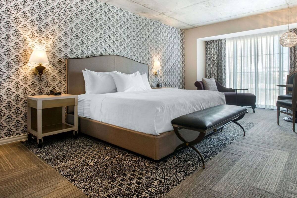 Ein Hotelzimmer mit einem großen Bett, Nachttischen, einer Bank, einem Sessel und einem Schreibtisch.