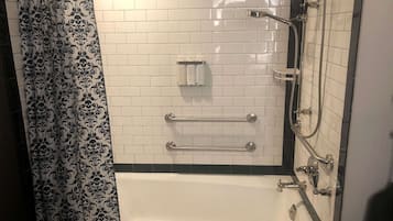 A bathroom with white tiled walls, a bathtub, a shower with a handheld showerhead, and a towel rack.