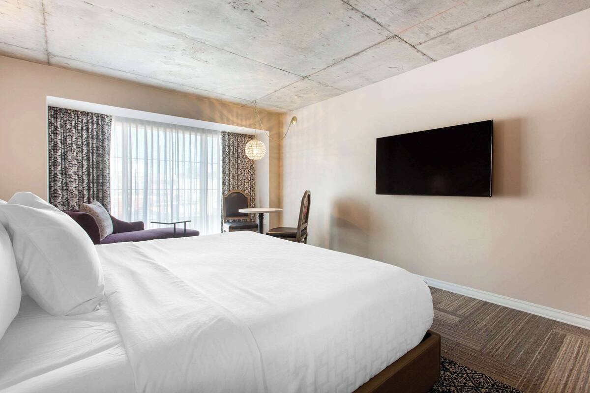 Una habitación de hotel con una cama grande, un televisor de pantalla plana en la pared, una mesita y una silla.