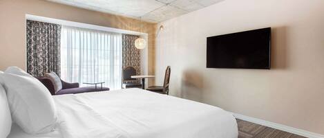 Una habitación de hotel con una cama grande, un televisor de pantalla plana en la pared, una mesita y una silla.