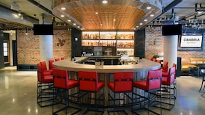 A bar area with a brick wall, a round bar counter, and red bar stools. - Cambria Hotel New Orleans Downtown Warehouse District (New Orleans)