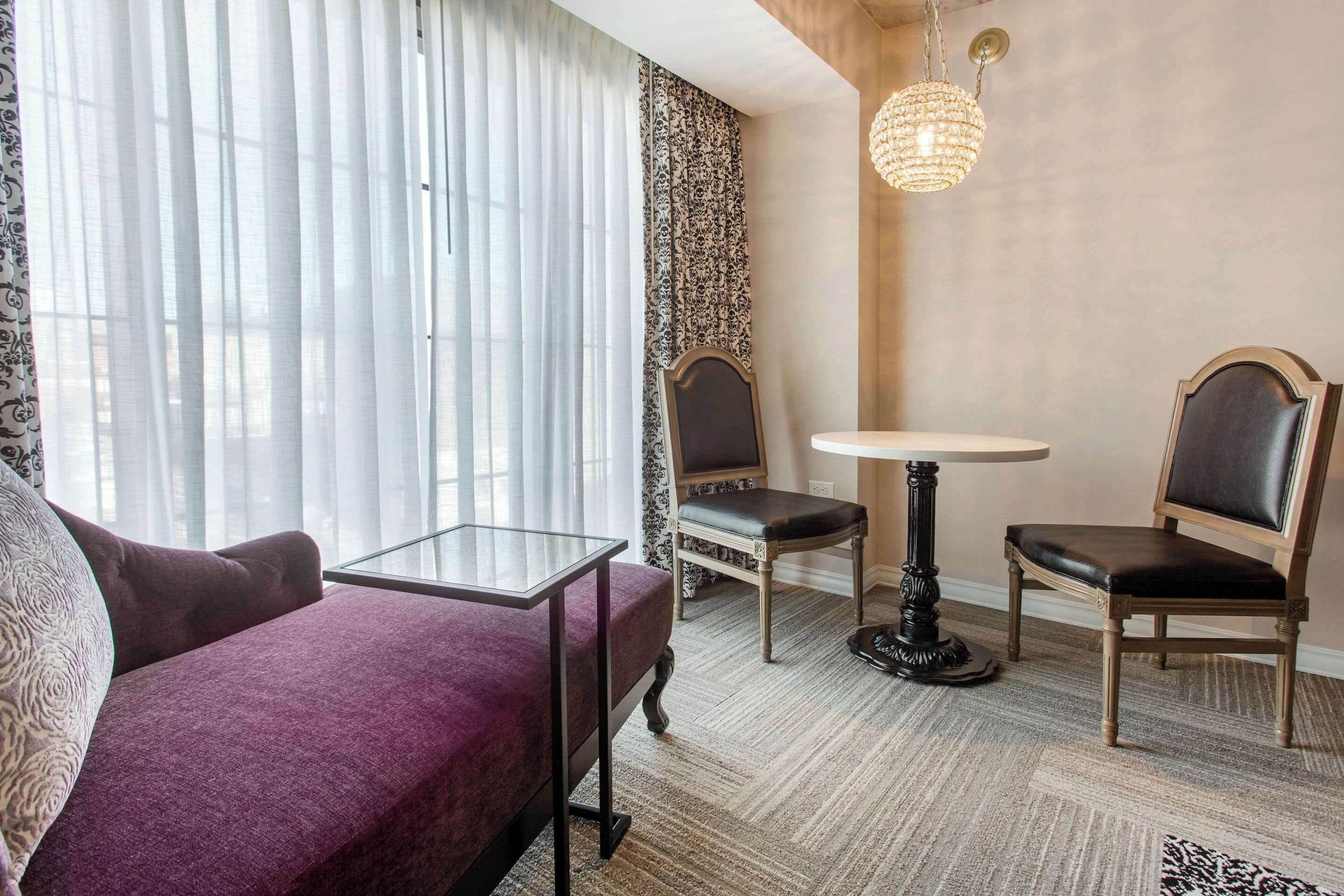 A hotel room with a purple sofa, two chairs, a small round table, and a chandelier.