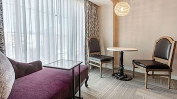 A hotel room with a purple sofa, two chairs, a small round table, and a chandelier.
