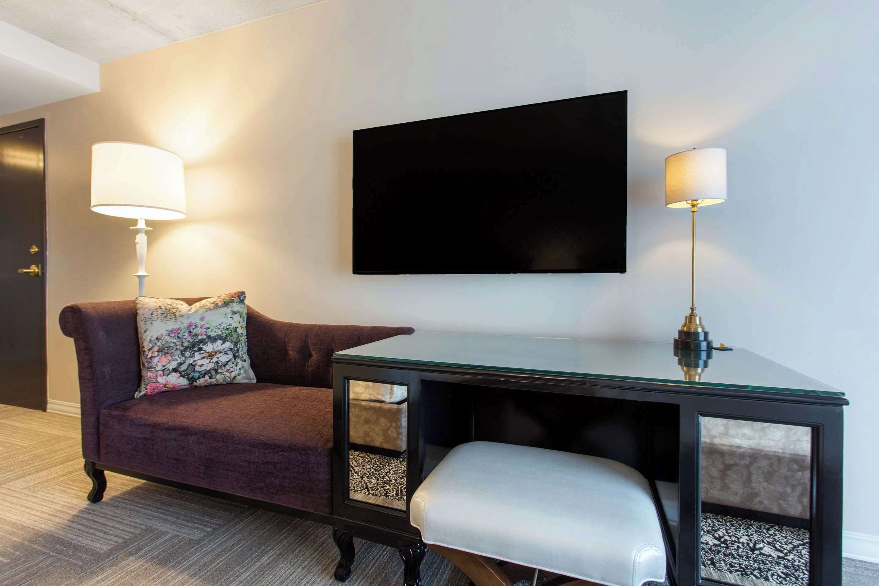 A modern room with a dark brown sofa, a glass-top table with a bench, and two wall-mounted lamps.