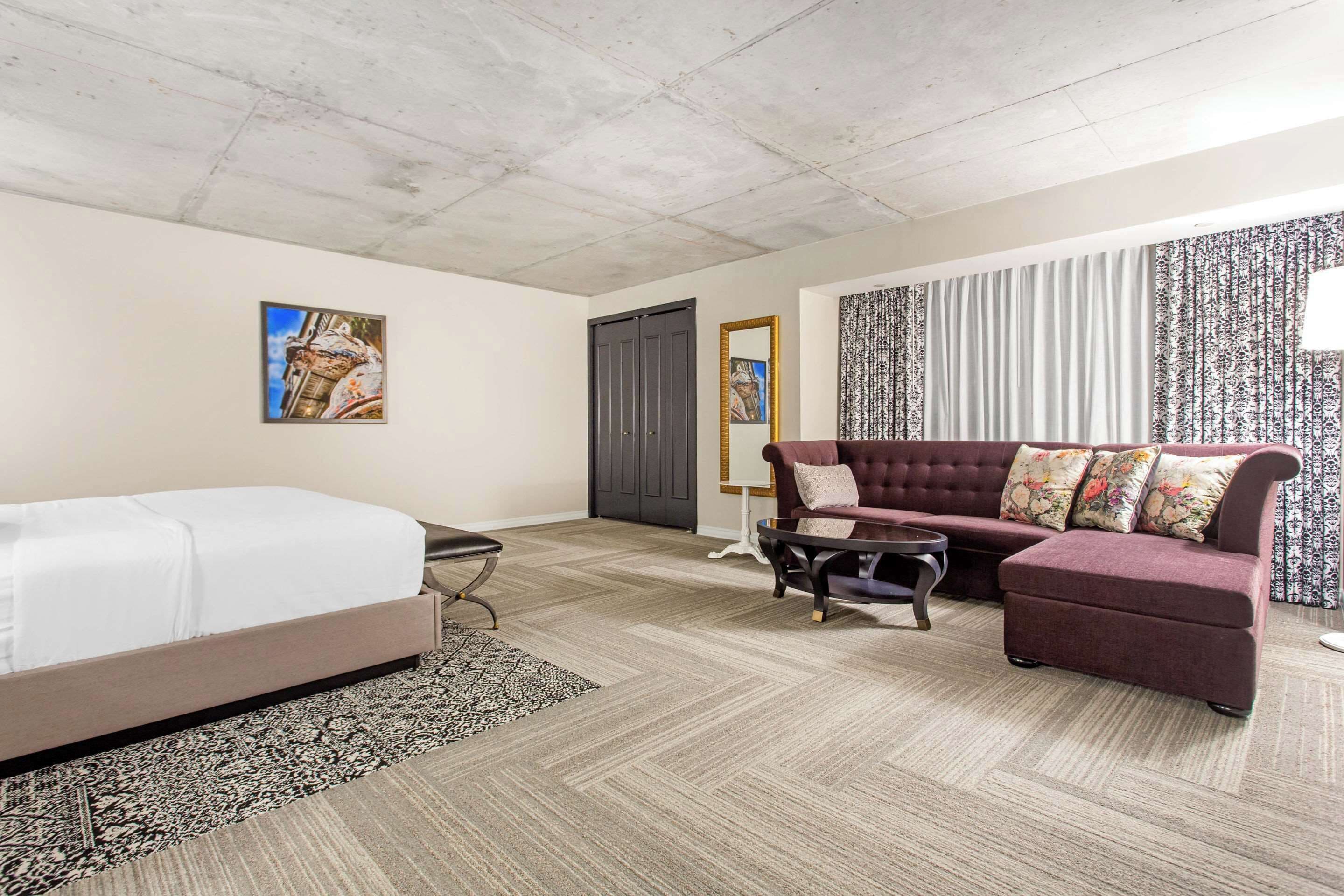 A hotel room with a bed, a sofa, a coffee table, and a patterned rug.
