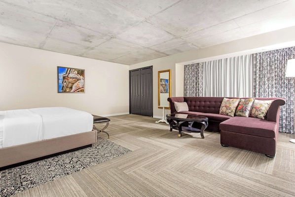 Una habitación de hotel con una cama, un sofá, una mesita de centro y una alfombra estampada.