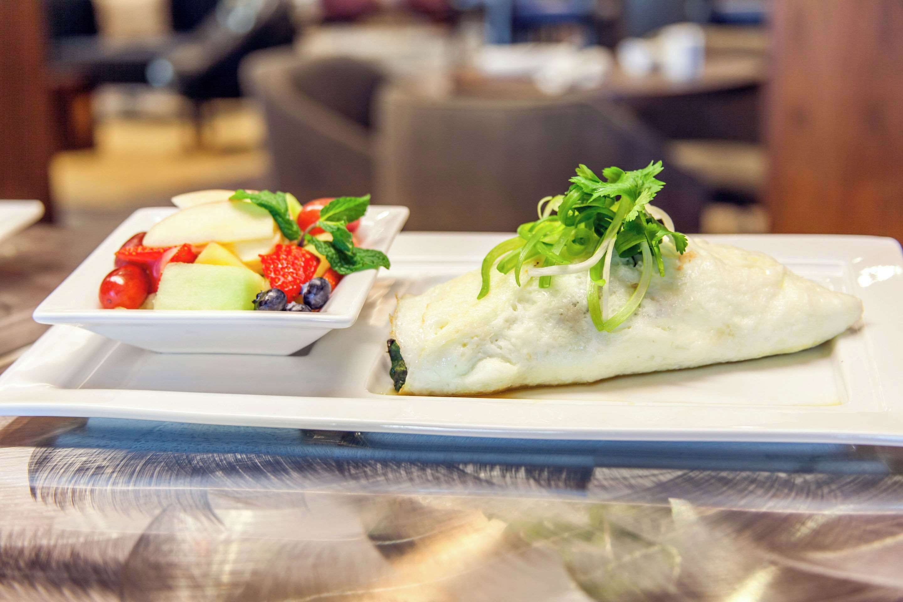 A white plate with a fish fillet garnished with green herbs and a side salad with strawberries, blueberries, and mint leaves.