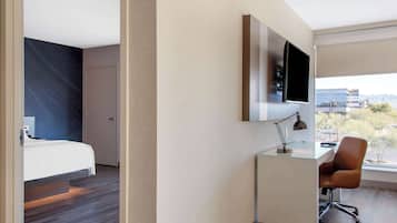 Una habitación de hotel moderna con cama, escritorio, silla, televisión y ventana con vistas a la ciudad.