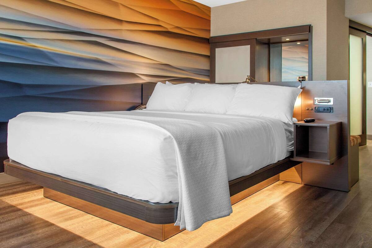 A modern hotel room with a bed, nightstand, and a wall mural.