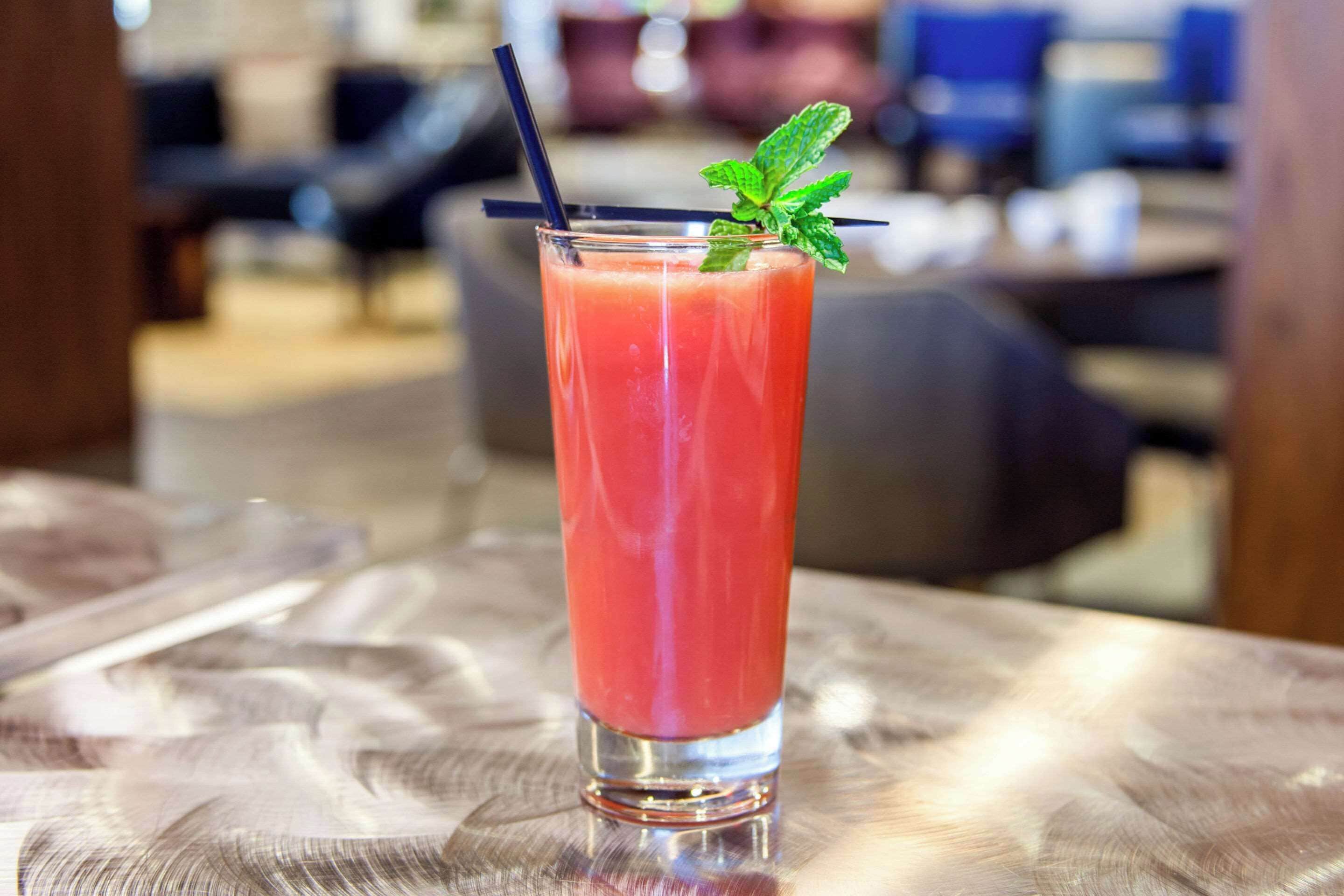 A tall glass with a red beverage, a black straw, and a mint garnish on a table.