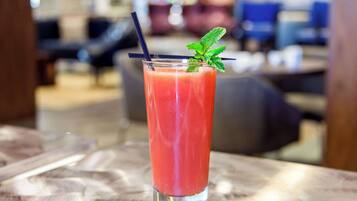 A tall glass with a red beverage, a black straw, and a mint garnish on a table.