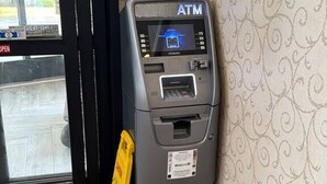 An ATM machine in a corner with a yellow caution sign, a door, and patterned wallpaper.