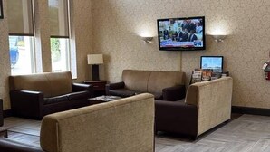 A hotel lobby with a large television screen, comfortable seating, and a patterned wall.