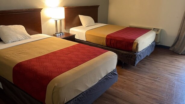 A hotel room with two beds, a nightstand, a lamp, and a window with curtains.