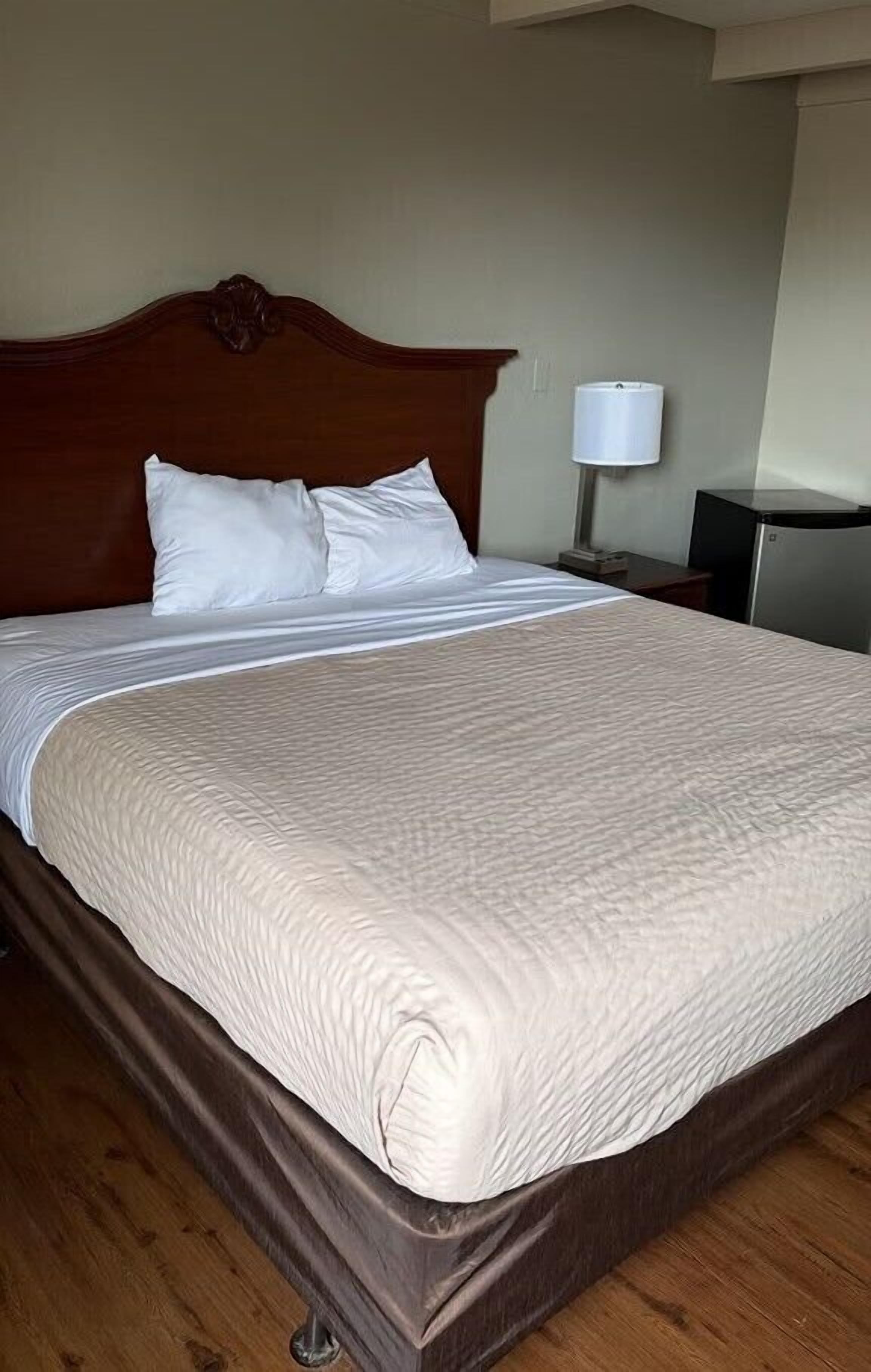 A neatly made bed with a wooden headboard, a white pillow, and a white blanket.