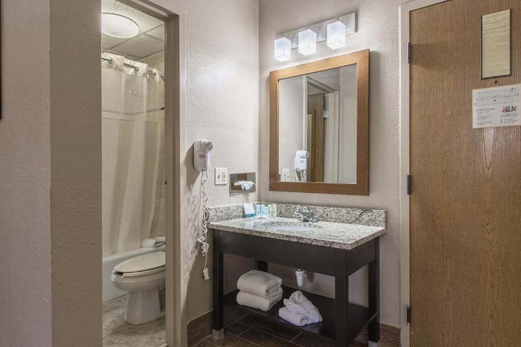 Un baño con ducha, inodoro y tocador con espejo y toallero.
