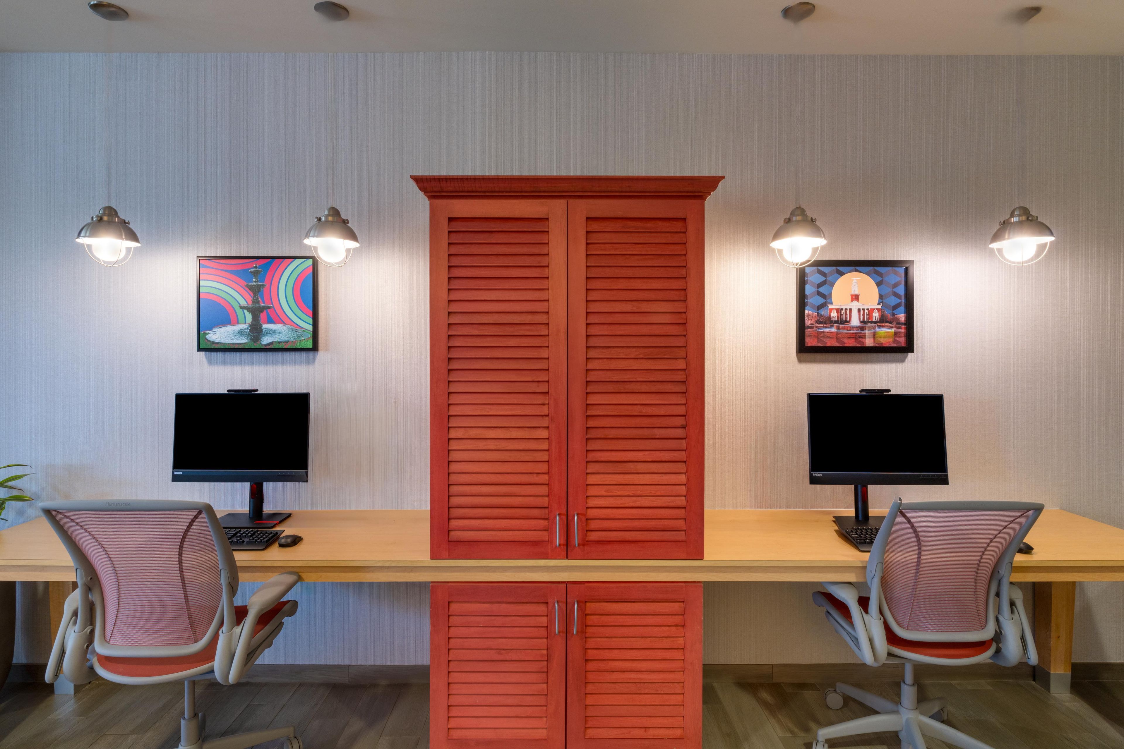 A room with two desks, each with a computer and chair, and two wall-mounted lamps.