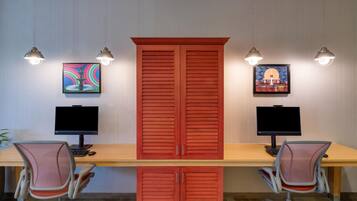 A room with two desks, each with a computer and chair, and two wall-mounted lamps.