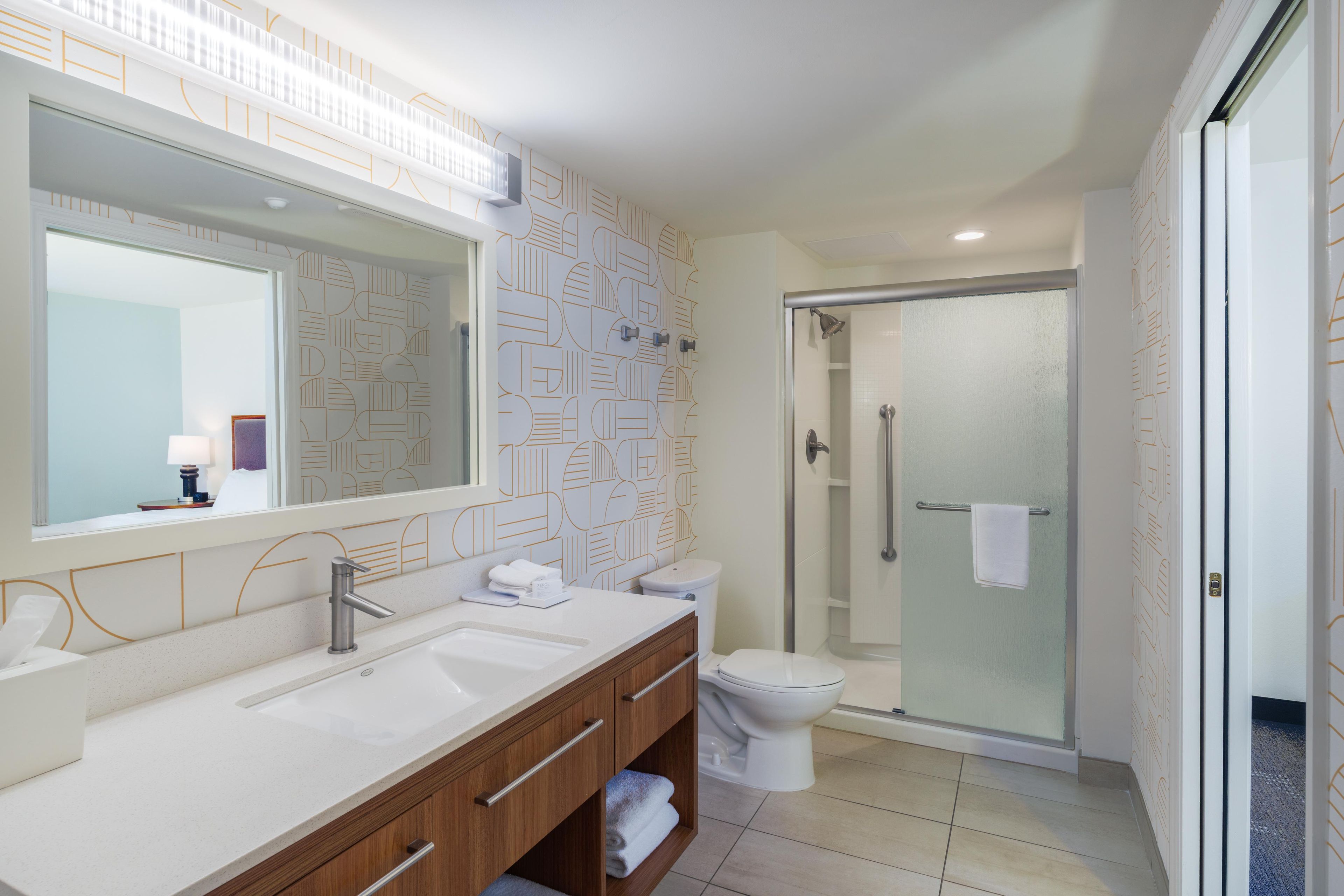 A modern bathroom with a large mirror, two sinks, a toilet, and a glass-enclosed shower.